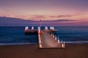 Aska Lara Resort & Spa Pier am Meer bei Sonnenuntergang mit roten Liegen und Laternen