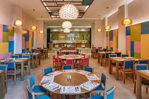 Innenbereich eines Restaurants im Aska Lara Resort & Spa mit bunten Wänden und runden Tischen.