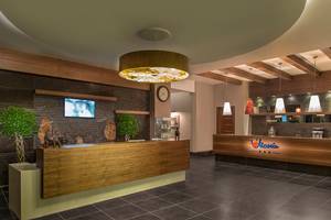 Rezeption im Aska Lara Resort & Spa mit Holzrezeptionstisch, Pflanzen und Bar.