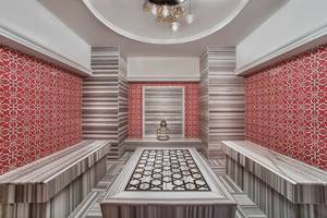 Innenbereich eines Spas im Aska Lara Resort & Spa mit roten und grauen Wandfliesen und einer zentralen Liegefläche.