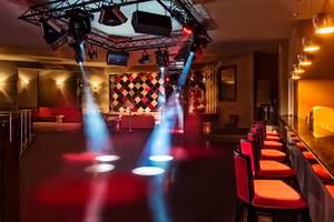 Ein Nachtclub mit roten Sitzen, einer Bar und Scheinwerferlicht.