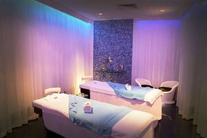 Massageraum im JA Ocean View Hotel mit zwei Massagetischen, blauen Kissen und weißen Stühlen.