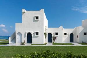 Außenansicht des Aeolos Beach Hotel auf Kos mit weißen Gebäuden, blauen Türen und grünem Rasen.