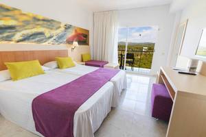 Helles Hotelzimmer im Moon Dreams Coral Beach mit zwei Betten, farbenfrohen Kissen und Blick auf die Landschaft.