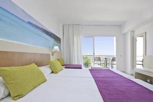 Ein helles Hotelzimmer im Moon Dreams Coral Beach mit zwei Betten und Blick auf das Meer durch große Fenster.