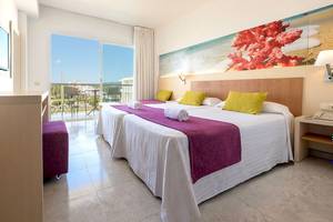 Helles Hotelzimmer im Moon Dreams Coral Beach mit zwei Betten, bunten Kissen und Blick auf die Terrasse.