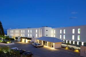 Außenansicht des Dimitra Beach Hotel & Suites bei Nacht mit beleuchteten Gebäuden und Autos im Parkbereich.