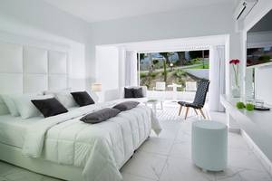 Schlafzimmer im Dimitra Beach Hotel & Suites mit weißem Bett und Möbeln, Balkonzugang und Gartenblick.