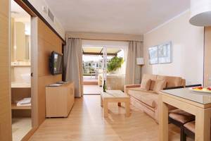 Wohnbereich des Zafiro Tropic Hotels mit Couch, Tisch, Fernseher und Glasfenstern.