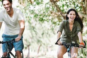 Mann und Frau radfahren lächelnd im Wald