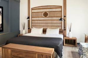 Ein modernes Hotelzimmer mit einem großen Bett, einem hölzernen Kopfteil, zwei Nachttischen und einer Gemäldewand.