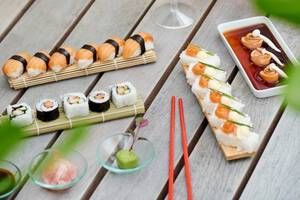 Mehrere Sushi-Platten und Beilagen auf einem hölzernen Tisch, darunter ein Glas Wein und verschiedene Saucen.