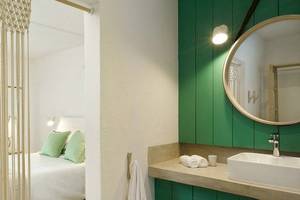 Innenansicht eines Zimmers im The Ravenala Attitude Hotel mit grünen Wänden, einem Bett, einem Spiegel und einem Waschbecken.