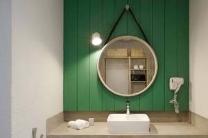 Badezimmer im The Ravenala Attitude Hotel mit grünen Wänden, einem runden Spiegel und einem weißen Waschbecken.