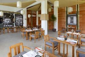 Innenansicht des Restaurants des Ravenala Attitude Hotels mit Holztischen, Stühlen und Dekoration.