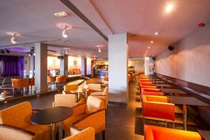 Innenbereich des Lanzarote Village Hotels mit orangen Stühlen und Tischen, Beleuchtung und einer Bühne.