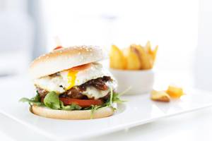 Ein Burger mit Ei auf einem weißen Teller mit Pommes