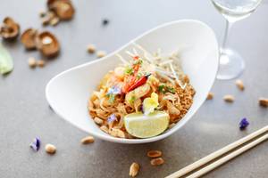 Asiatisches Gericht in einer weißen Schale mit Limettenscheibe und Beilagen wie getrockneten Pilzen und Nüssen