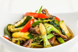Ein weißer Teller mit asiatischem Gemüse, einschließlich Paprika, Zucchini und Brokkoli.