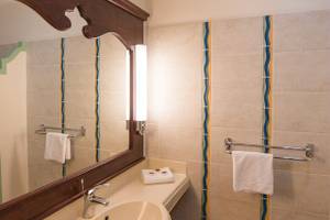 Badezimmer im Pierre & Vacances Village Sainte Luce mit Spiegel, Waschbecken, Handtüchern und Wandmustern.