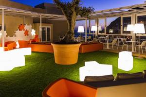 Abendliche Hotelterrasse mit Sitzmöbeln, Lampen und Blick aufs Meer.