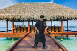 Ein Mitarbeiter des Kurumba Maldives Hotels steht auf der Terrasse und lächelt in die Kamera.