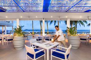 Innenansicht des Kurumba Maldives Restaurants mit Blick auf den Ozean und einem Kellner, der einen Tisch bedient.