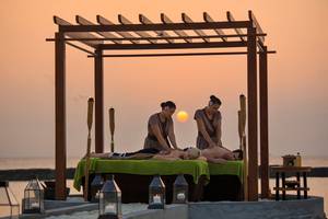 Massage unter einem Pavillon am Strand im Kurumba Maldives bei Sonnenuntergang.