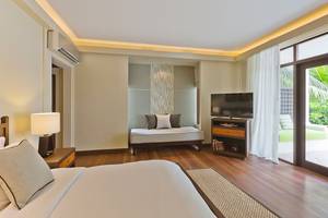 Schlafzimmer im Kurumba Maldives Hotel mit Doppelbett, Fernseher, Nachttisch und Fenstern.