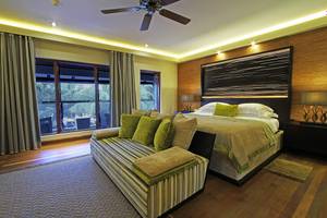 Schlafzimmer im Kurumba Maldives Hotel mit großem Bett, Fenstern und Holzboden.