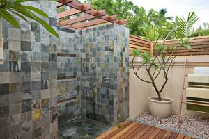 Außenbereich der Dusche im Kurumba Maldives Hotel mit Steinwand und Holzpergola.