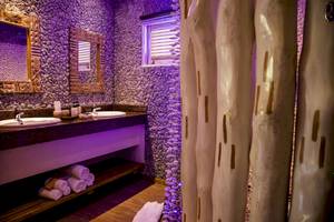 Badezimmer im Le Domaine de L'Orangeraie Resort & Spa mit violetten Wänden, zwei Waschbecken und vielen Handtüchern.