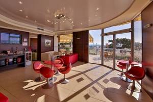 Loungebereich des Kaliakra Beach Hotels mit roten Stühlen und Tischen, Fernseher und Panoramafenstern