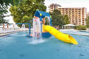 Wasserrutsche im Außenbereich des Kaliakra Beach Hotels mit grünen Bäumen und Gebäude im Hintergrund.