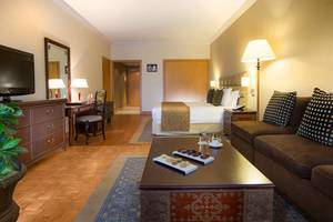 Innenansicht einer Hotelsuite im Millennium Plaza Downtown mit Bett, Wohnzimmer und Schreibtisch.