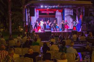 Eine Gruppe von Künstlern führt eine Show auf der Bühne des Lopesan Costa Meloneras Resorts & Spa auf, während das Publikum zuschaut.