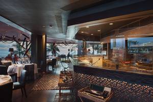 Innenansicht eines Hotelrestaurants mit Blick auf das Meer, Tische und Stühle sind sichtbar.