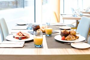 Frühstückstisch im Novotel London Blackfriars mit Pfannkuchen, Croissants, Brötchen und Orangensaft.
