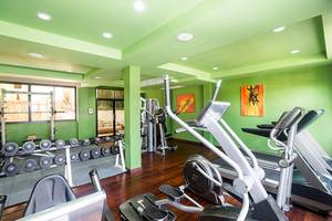 Fitnesscenter im Khao Lak Laguna Resort mit grünen Wänden, Laufbändern, Hanteln und Gemälden.