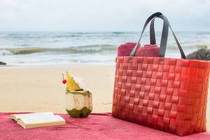 Rote Strandtasche mit Kokosnuss und Buch am Strand