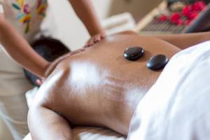 Eine Massagebehandlung im Sandos Caracol Eco Resort, bei der eine Person mit schwarzen Steinen auf dem Rücken liegt.