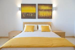 Schlafzimmer mit Doppelbett im Agua Hotels Sal Vila Verde, weiße Wände, zwei Gemälde, gelbe Vorhänge und Nachttische.