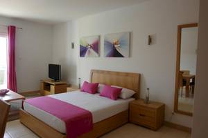 Schlafzimmer im Agua Hotels Sal Vila Verde mit einem großen Bett, Fernseher, Nachttischen und Gemälden an der Wand.