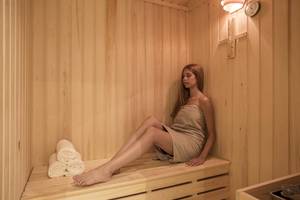 Frau sitzt entspannt in der Sauna des Aeolos Beach Resorts auf Korfu, mit drei Handtüchern auf der Bank.