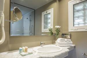 Badezimmer im Aeolos Beach Resort auf Korfu mit Spiegel, Waschbecken und Toilettenartikeln.