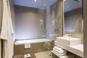 Badezimmer im Aeolos Beach Resort auf Korfu mit Badewanne, Dusche, Waschbecken und Handtüchern.