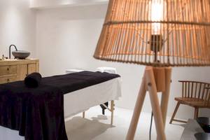 Spa-Behandlungsraum im Aeolos Beach Resort Hotel mit Behandlungstisch, Lampe und Holzmöbeln.