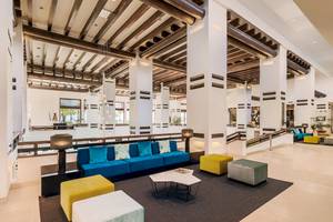 Innenansicht des H10 Estepona Palace Lobbys mit blauem Sofa und gelben Hockern.