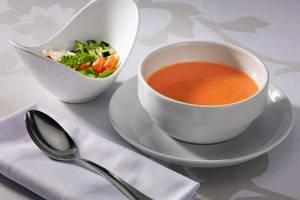 Ein weißer Teller mit einer weißen Schüssel Tomatensuppe und Salat.