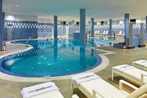 Indoorpool des H10 Estepona Palace mit Loungebereich und weißen Liegen.